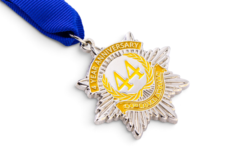 Silver 4-year anniversary medal with yellow enamel details, a starburst design and a blue ribbon for the Royal Anglian Regiment.