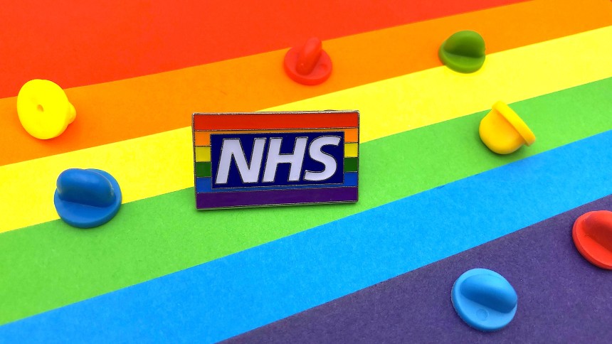 An NHS pride flag pin badges sat on a multicoloured background with rubber clutches of al the colours of the rainbow.
