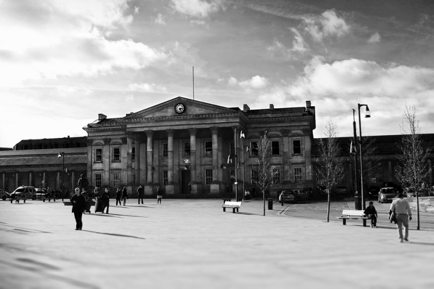A black & white photo of Huddersfield train station and people going about their business.