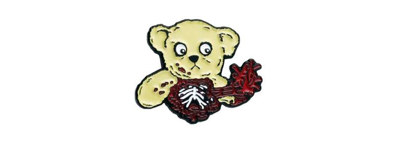 A pin badge of a teddy bear who has ripped his own heart out and is staring at it with maniacal eyes.