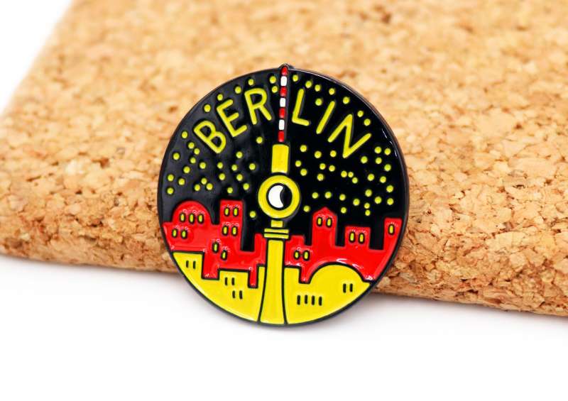 A circular pin badge featuring landmarks of Berlin. The cityscape is in the colours of the German flag.