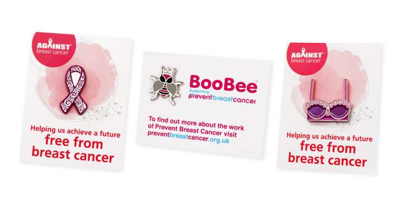 Three charity enamel pin badges to help raise money for breast cancer. The badges are a pink awareness ribbon, a bee, and a bra.