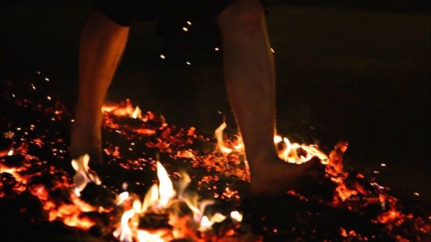 A barefooted fore walker saunters across red hot coals.