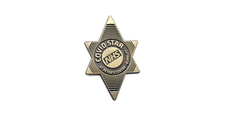 A gold star die struck badge with the NHS logo and the words 