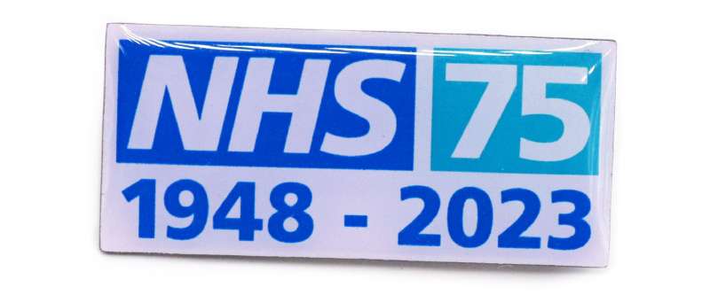 A pin badge of the NHS 75th birthday logo. It features the NHS logo, the number 75 and the date 1948 - 2023 underneath.