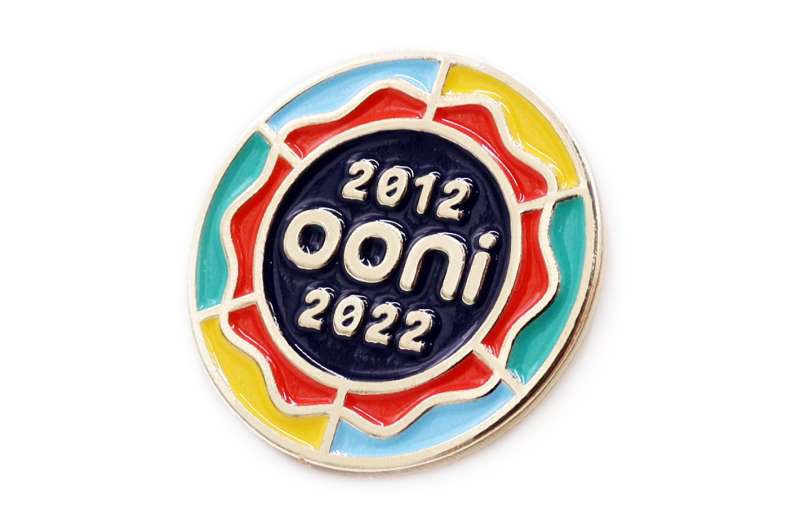 An Ooni pin badge with their logo and the dates 2012 - 2022. It seems like a pizza but the colours are yellow, green, red, and white blue.