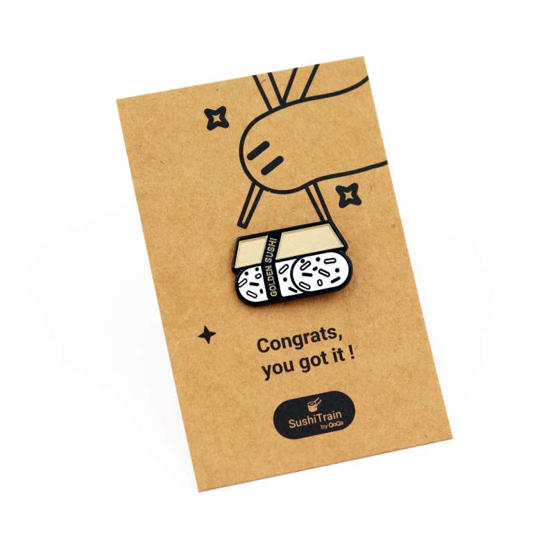 A sushi pin badge on a brown backing card with a cats paws holding chopsticks.