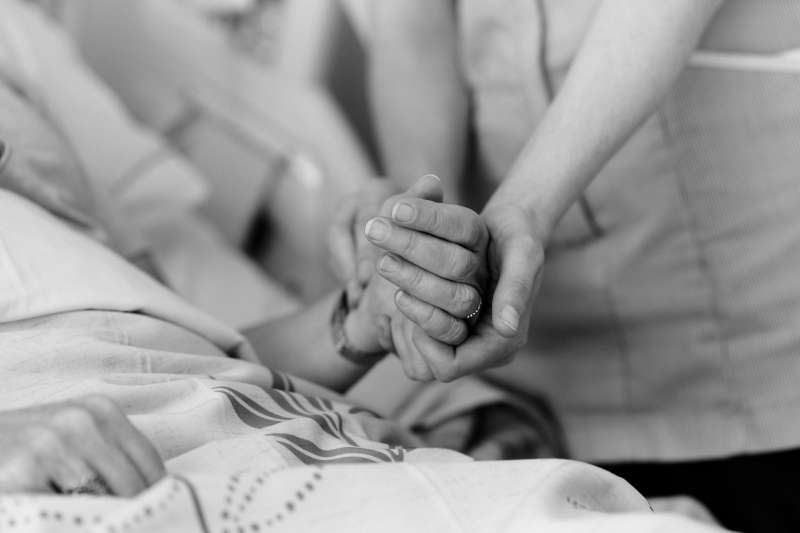 Two people holding hands as one comforts the other in a hospital bed.