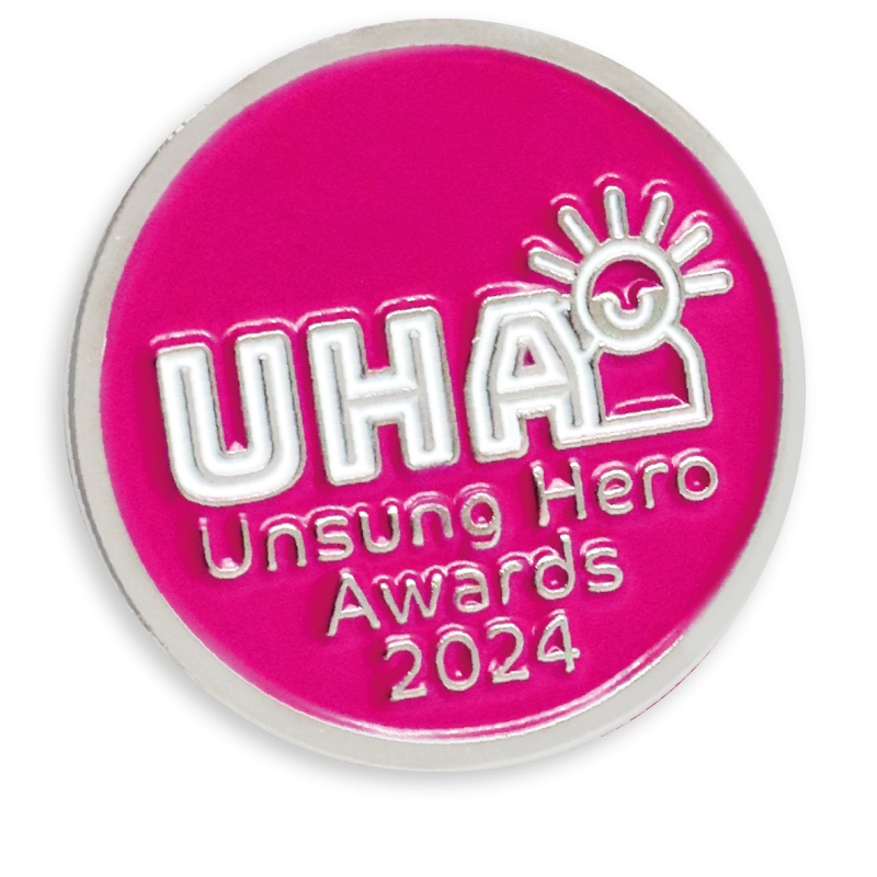 The official Unsung Hero Award pin badge with pink background and silver plating.