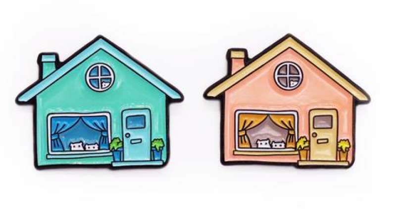 Two enamel pins of a identical house that have a door, a rectangular window, and a round window upstairs. One house is aqua blue, the other is peach coloured.
