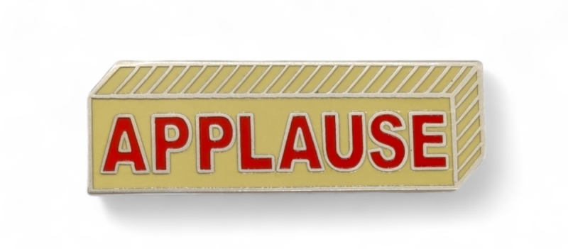 A retro-style applause enamel pin with vintage feel. The badge looks like an applause sign with red letters.