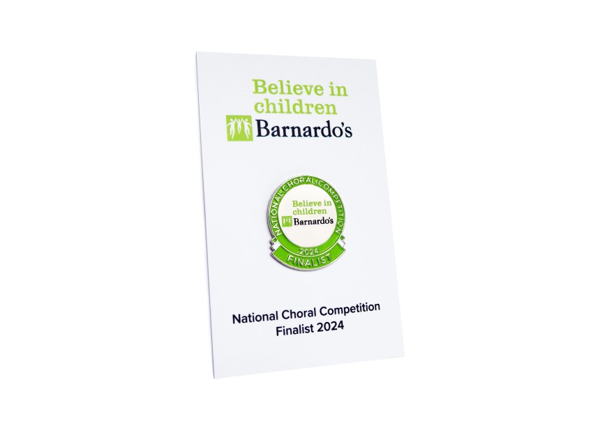 A Barnardo's special edition pin badges to commemorate the National Choral Competition of 2024. The green and silver pin badge is fastened to a white backing card with green and black text.