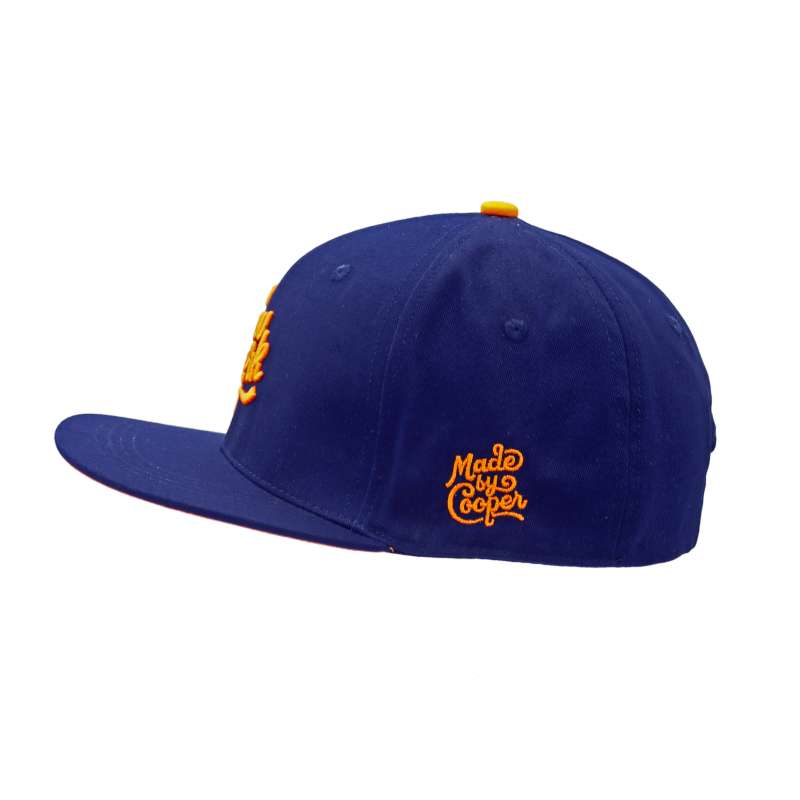 A side shot of a blue baseball cap with an orange Made by Cooper logo and orange button.