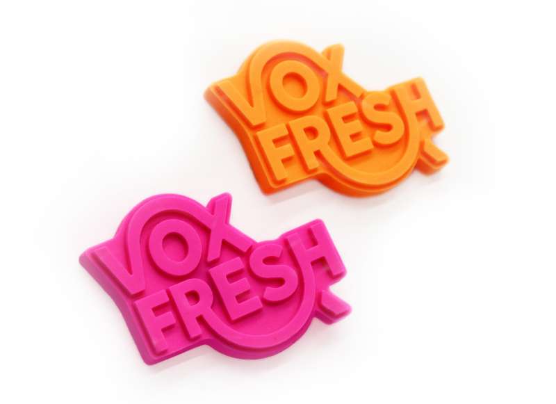 Two PVC custom pin badges featuring the Vox Fresh logo. One badge is bright orange and the other is a vibrant pink.