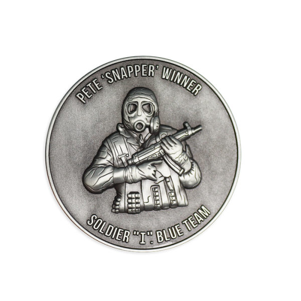 A silver custom challenge coin featuring the 3D design of a soldier holding a MP5 submachine gun. The words