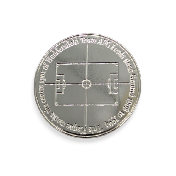 A circular bespoke die struck badge with the outline of a football pitch on it.