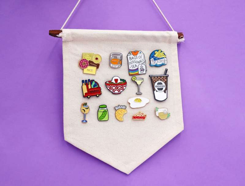 A cloth display banner with a selection of 14 pin badges in the food and drink theme.