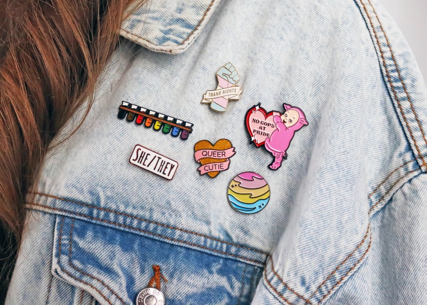 A denim jacket displaying six LGBTQ+ pin badges.