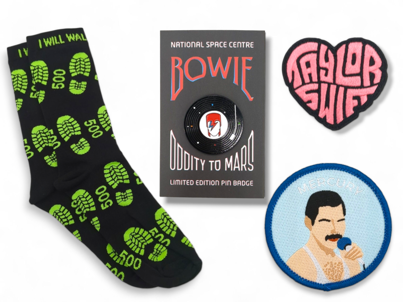 Fan-inspired custom music merch featuring Proclaimers socks, a David Bowie pin badge, and patches for Taylor Swift and Freddie Mercury.