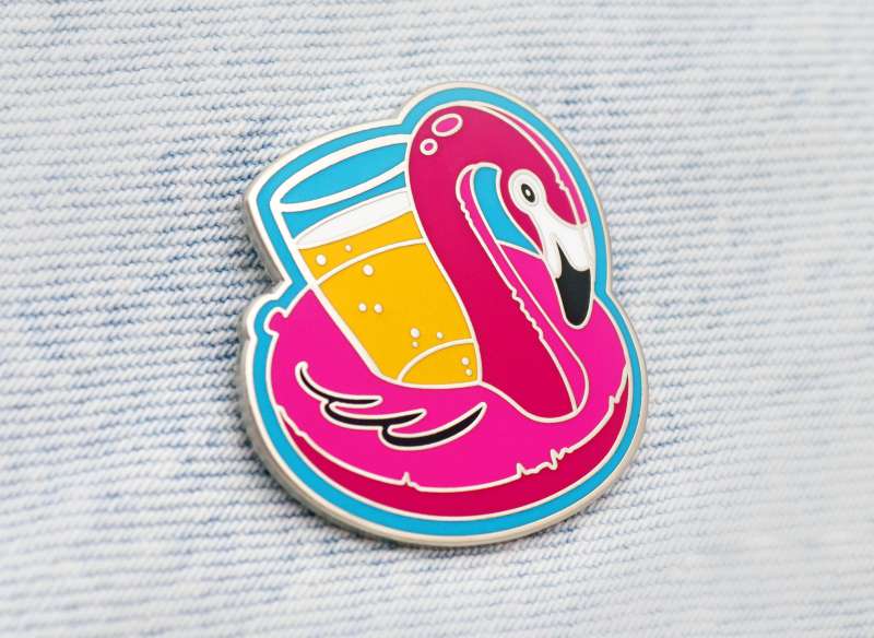 A vibrant pin badge of a pink flamingo inflatable carrying a cold pint of delicious lager.