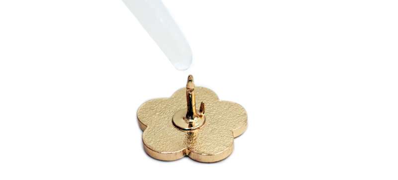 A gold pin badge spike with super glue being applied to it.