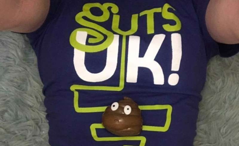 Someone laid down wearing a Guts UK T-Shirt and they have a plastic poo with eyes on her belly.