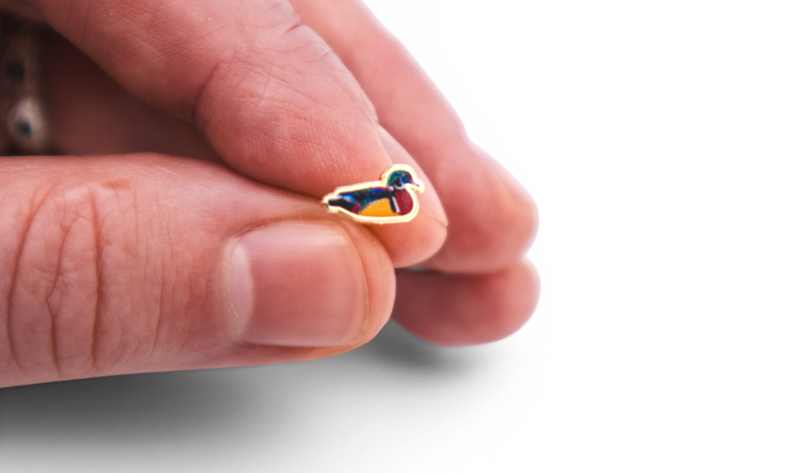 Tiny duck enamel pin badge held between two fingers, showing how a miniature pin design looks at its finished physical size.