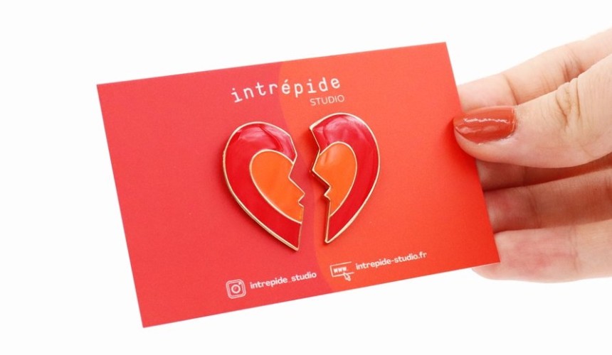 A broken heart pin badge on a red backing card