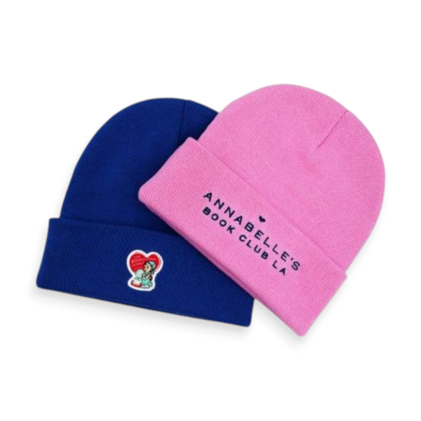 A bright pink and a navy blue beanie with embroidered logos to advertise a book club.