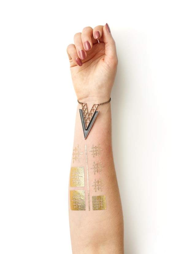 A lady's arm featuring a triangular bracelet and some geometrically patterned fake tattoos.
