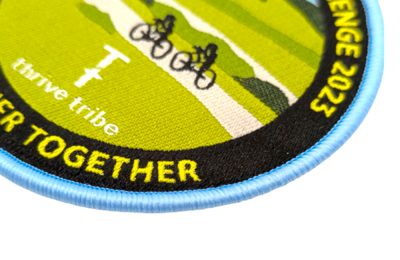 A close-up of a woven cycling patch with a light blue overlocked border.