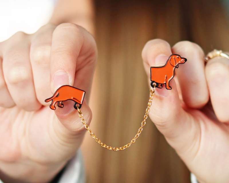 A sausage dog pin badge that's split into two and connected by a chain so you can use it as a fashion accessory.