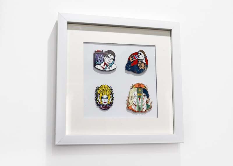 A white pin badge display frame featuring four horror enamel badges from Nacho Scratcho.