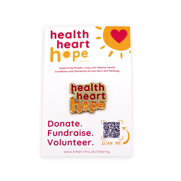 Soft enamel charity pin badge featuring the Health Heart Hope logo in red and orange enamel, displayed on an NHS charity backing card promoting donations, fundraising and volunteering for mental health and dementia support.
