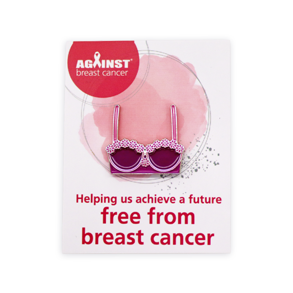 Soft enamel pin badge featuring a pink bra design displayed on an Against Breast Cancer backing card, created as a charity awareness pin badge with raised metal lines and coloured enamel fill.