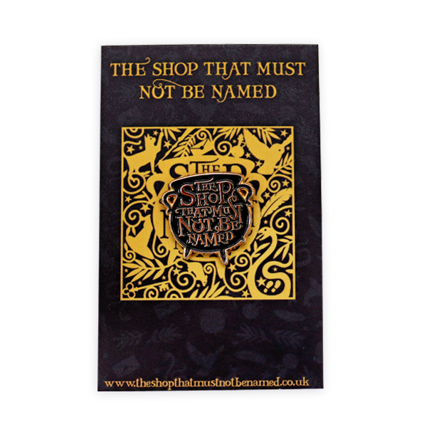 Soft enamel pin badge displayed on a decorative backing card reading “The Shop That Must Not Be Named”, featuring ornate gold artwork and raised enamel details for a collectible pin badge.