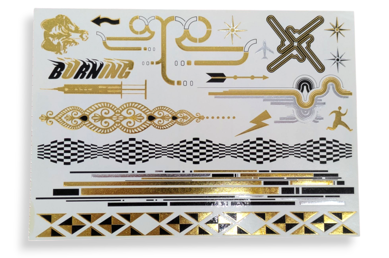 A sheet of metallic fake festival tattoos featuring bold geometric shapes, tribal patterns, a syringe, and the word burning that looks like it is on fire.