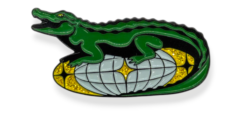 A pin badge featuring the Lacoste crocodile sitting on top of a glittery discoball.
