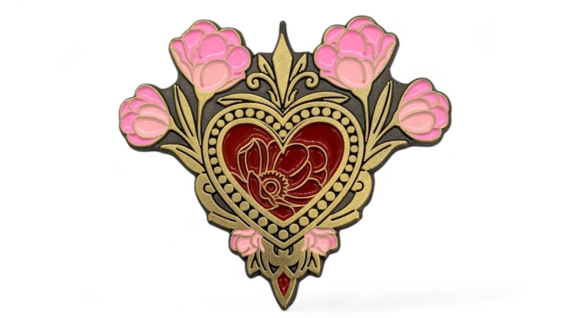 A brass antique enamel pin with love heart in the middle that's surrounded by pink flowers.