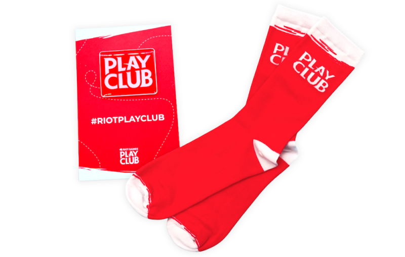 Riot Games Play Club red-branded socks with promotional pin badge and backing card for gaming community merch.