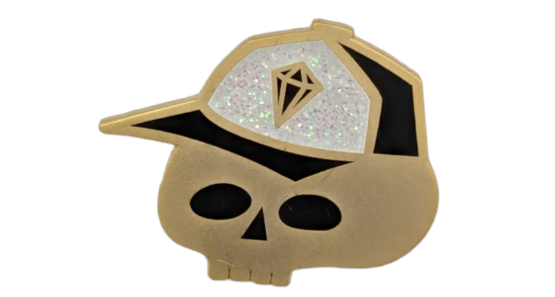 A matt gold skull pin badge wearing a cap with a glitter enamel background.