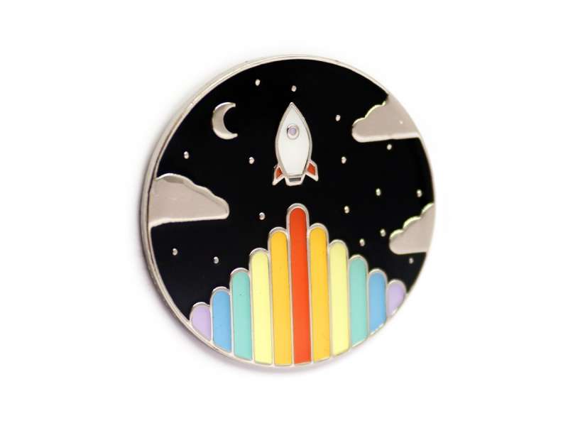 A beautiful hard enamel pin badge featuring a space rocket and rainbow coloured blast off!