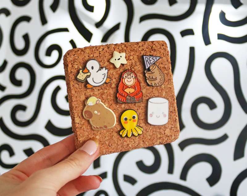A collection of themed cute pin badges position on a small cork coaster. The Made by Cooper pattern sits in the background.