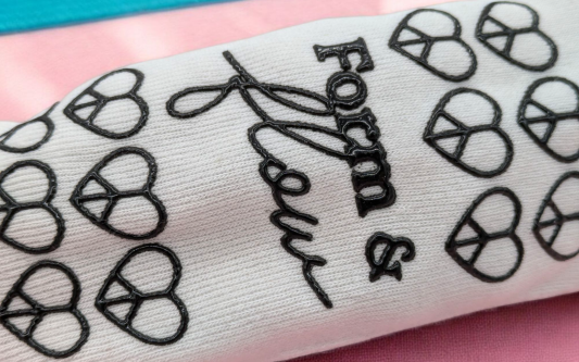 A white pilates sock with a black patterned grip on the sole. The pattern is hearts with the words