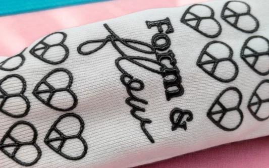 A white pilates sock with a black patterned grip on the sole. The pattern is hearts with the words