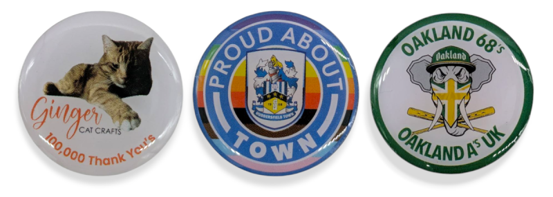 Three round printed pin badges featuring a realistic cat, the Huddersfield Town Football Club crest with