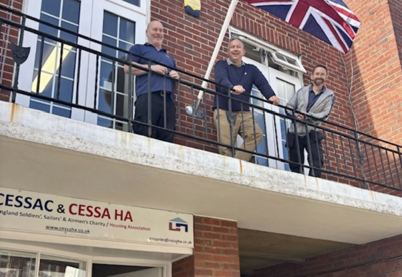 Three members of the CESSAC organisation standing on a balcony above the headquarters main entrance.
