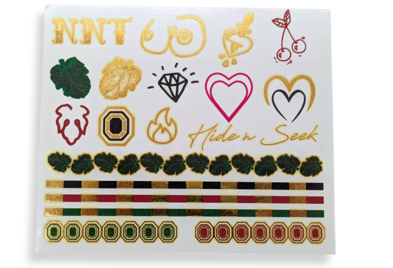 A sheet of metallic festival fake tattoos featuring arm bands, a diamond, hearts, and a pair of boobs.