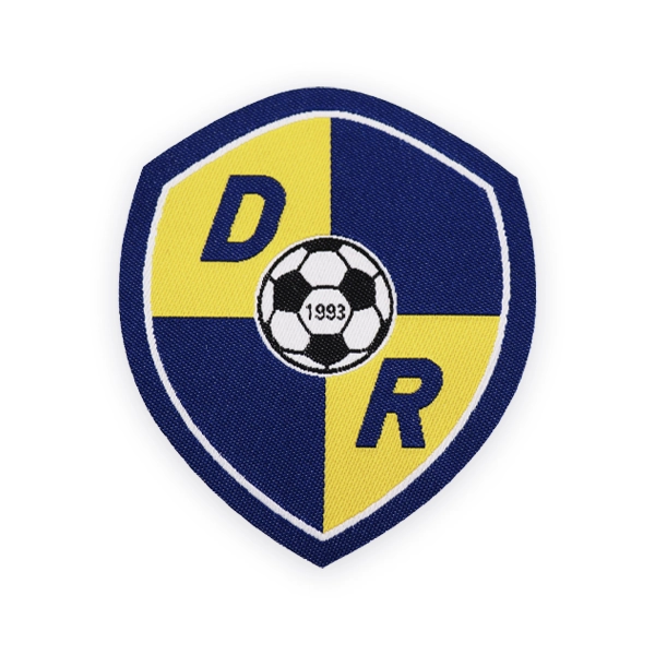 Shield shaped woven patch displaying a football crest with blue and yellow quarters, central football icon and initials, designed as a durable custom woven patch for sports teams and club uniforms.