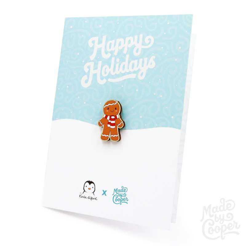 A gingerbread man wooden pin badge and a baby blue and white Christmas card that reads 